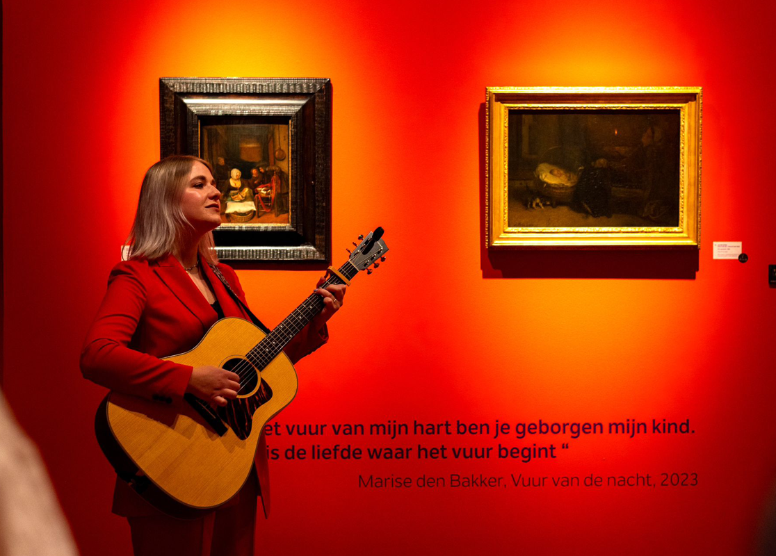Zangeres Marise staat met gitaar voor kunstwerken in de museumzaal